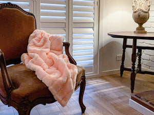 A plush pink faux fur throw blanket draped over a brown armchair.